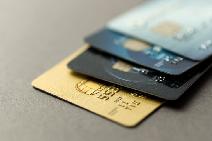 Four credit cards piled on top of each other on a table. The bottom card is gold. The top cards are black, blue, and silver.